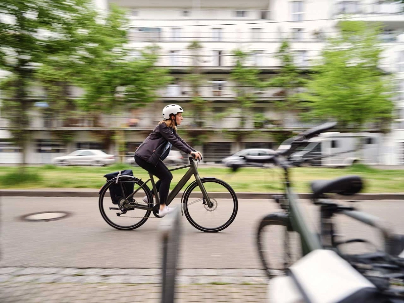 Eine Radfahrerin in Bürokleidung fährt die Straße entlang, Sie hat ihre Tasche am Hinterradblech ihres Fahrrads befestigt