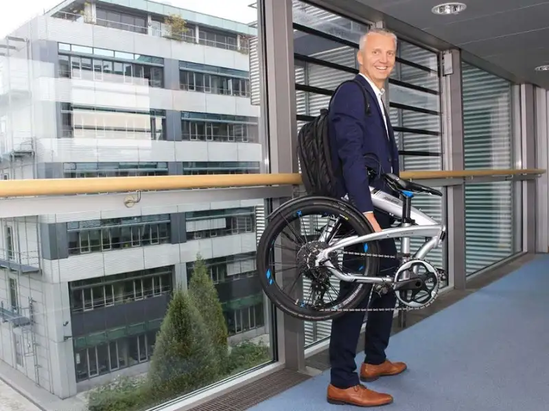 Mitarbeiter mit Faltrad gefaltet - Frank Noe Mitarbeiter mit Faltrad gefaltet - Frank Noe